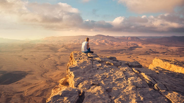 a man sitting on the edge of mitzpe ramon crater in israel